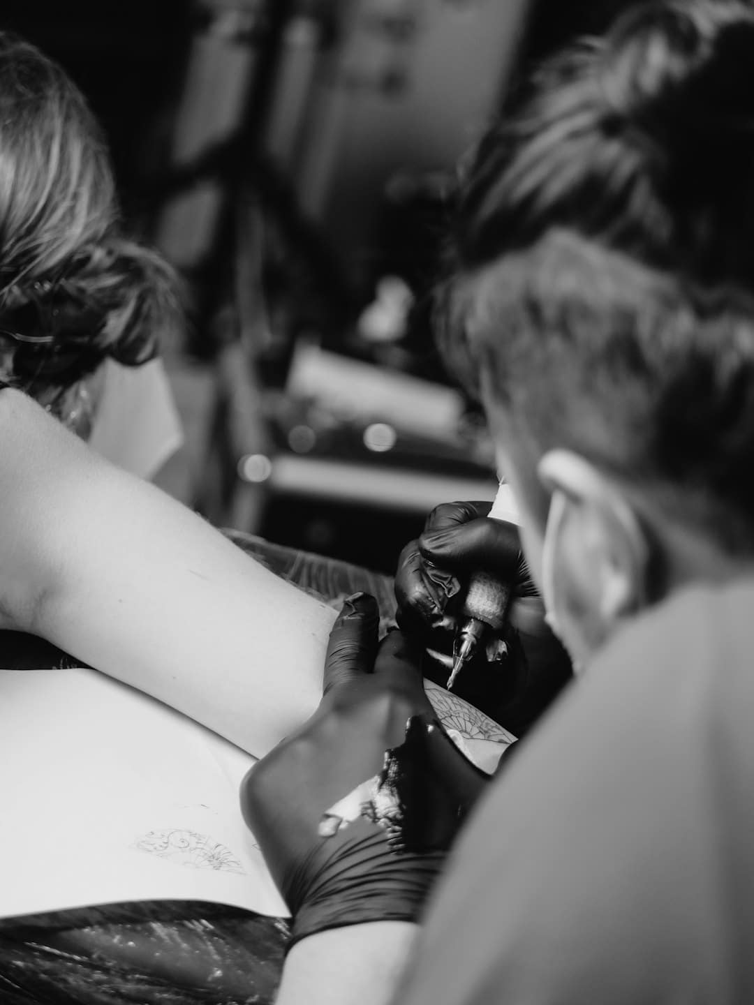 Tattoo artist working on client's forearm in studio.